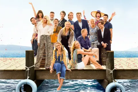 Obsada filmu "Mamma Mia!" na drewnianym molo z widokiem na morze.