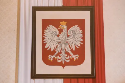 Orzeł Biały w koronie na czerwonej tarczy, symbol Polski. W tle biało-czerwone zasłony. Jakoś to będzie, nawet w trudnych czasach.