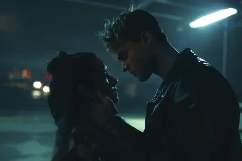 Nocna scena z filmu "The Kissing Booth". Elle i Noah w intymnym uścisku, w tle migoczące światła samochodów.