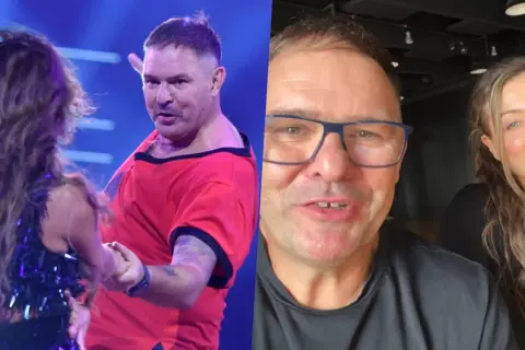 Tomasz Karolak tańczy na scenie w czerwonej koszulce i pozdrawia z uśmiechem w okularach. Obok niego uśmiechnięta kobieta.