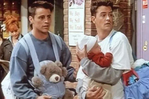 Chandler Bing z niemowlakiem i Joey z misiem w nosidle.