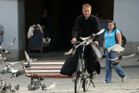 Ojciec Mateusz na rowerze, otoczony przez stado gołębi.