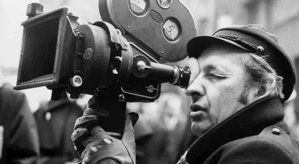 Andrzej Wajda patrzy przez wizjer kamery filmowej.