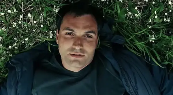 Mężczyzna leży na trawie, otoczony zielenią i białymi kwiatkami. Może to scena z filmu, gdzie wino truskawkowe obsada odgrywa ważną rolę.