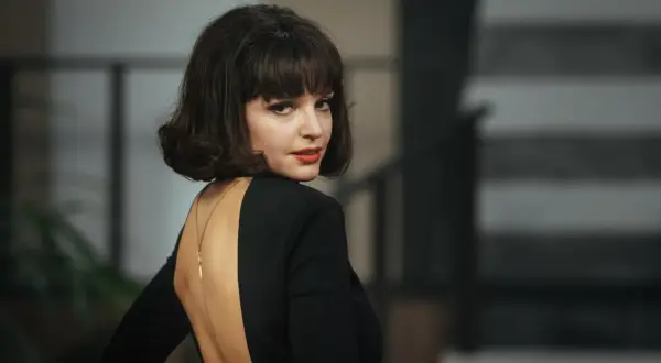 Elegancka Maria Dębska w czarnej sukni z głębokim wycięciem na plecach, zmysłowo odwraca głowę.