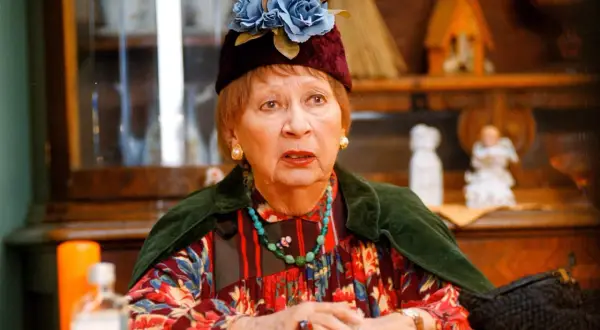 Irena Kwiatkowska w ozdobnym kapeluszu z kwiatami, w kolorowej sukience i z naszyjnikiem.