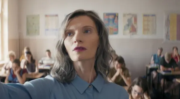 Nauczycielka w klasie, w tle widać innych ludzi, obsada filmu.