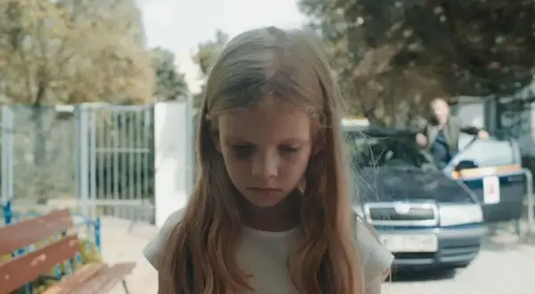 Smutna dziewczynka z sińcami pod oczami, w tle samochód i mężczyzna. Scena z filmu budząca konfuzję.
