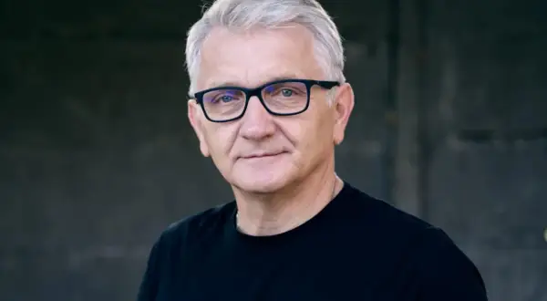 Portret Dariusza Kowalskiego, aktora, w okularach i czarnej koszulce.