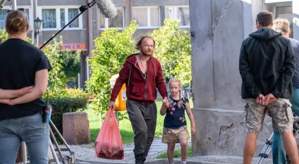 Mężczyzna z dziewczynką idą ulicą, za nimi ekipa filmowa z mikrofonem.