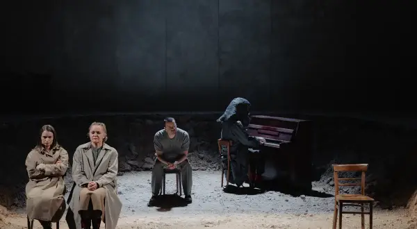 Trzy osoby siedzą na krzesłach. Jedna gra na pianinie, ubrana w kaptur. Jutro jest nasze.