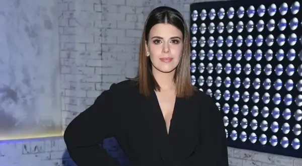 Monika Mazur w czarnym eleganckim stroju pozuje na tle ceglanej ściany i panelu z niebieskimi światłami.