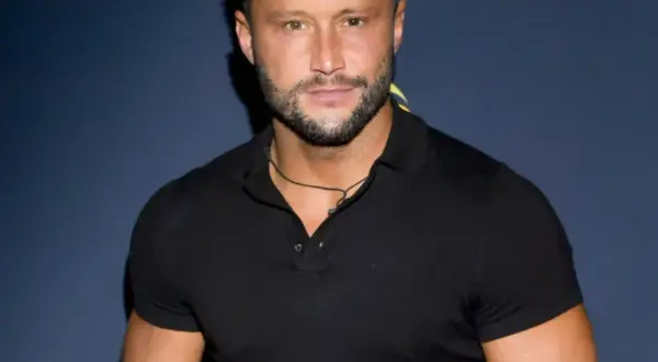 Piotr Mróz w czarnej koszulce polo, z zarostem i naszyjnikiem.