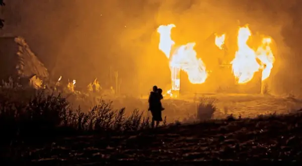 Płonące domy na Wołyniu. Sylwetka matki z dzieckiem na rękach obserwuje tragedię.