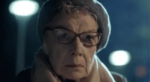 Aleksandra Górska w okularach i czapce, zamyślona, w świetle latarni.