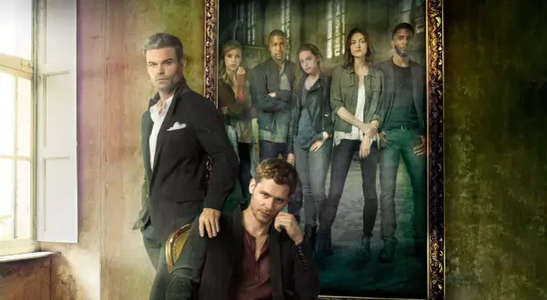 Grupowe zdjęcie obsady "The Originals" w stylizowanych strojach. W pierwszym planie siedzi Klaus, a za nim stoi Elijah. W tle, w ramie obrazu, widać pozostałych członków rodziny.