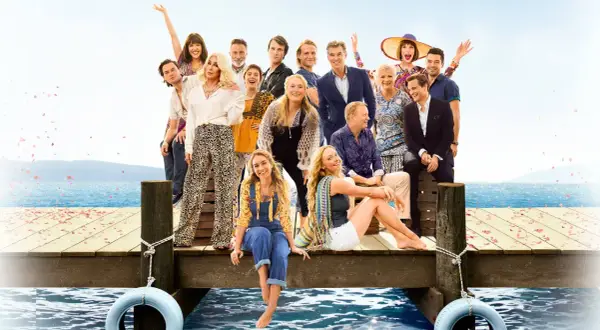 Obsada filmu "Mamma Mia!" na drewnianym molo z widokiem na morze.