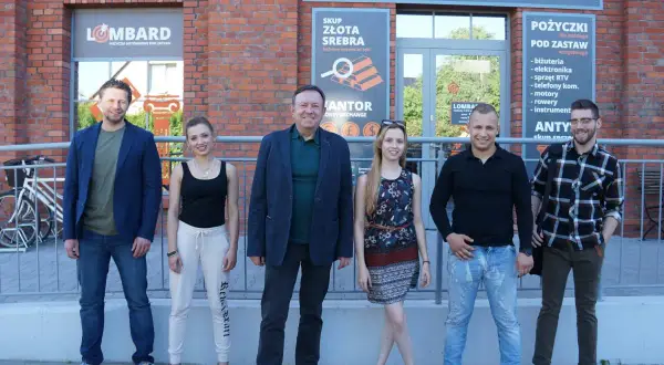 Aktorzy z lombardu pozują przed budynkiem.