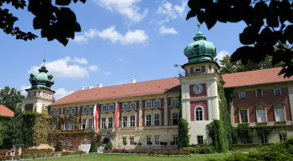 Pałac z zielonymi kopułami i zegarem, ozdobiony flagami, otoczony ogrodem.