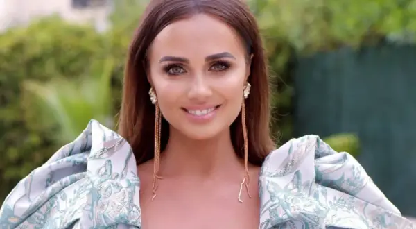 Uśmiechnięta Agnieszka Mrozińska w eleganckiej sukni z bufiastymi rękawami i długimi kolczykami.