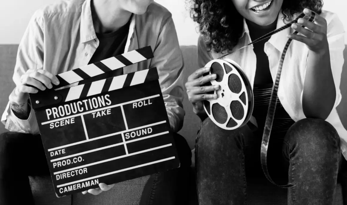 Dwie osoby z klapsem filmowym i rolką taśmy filmowej. Zastanawiasz się, ile zarabia producent filmowy?