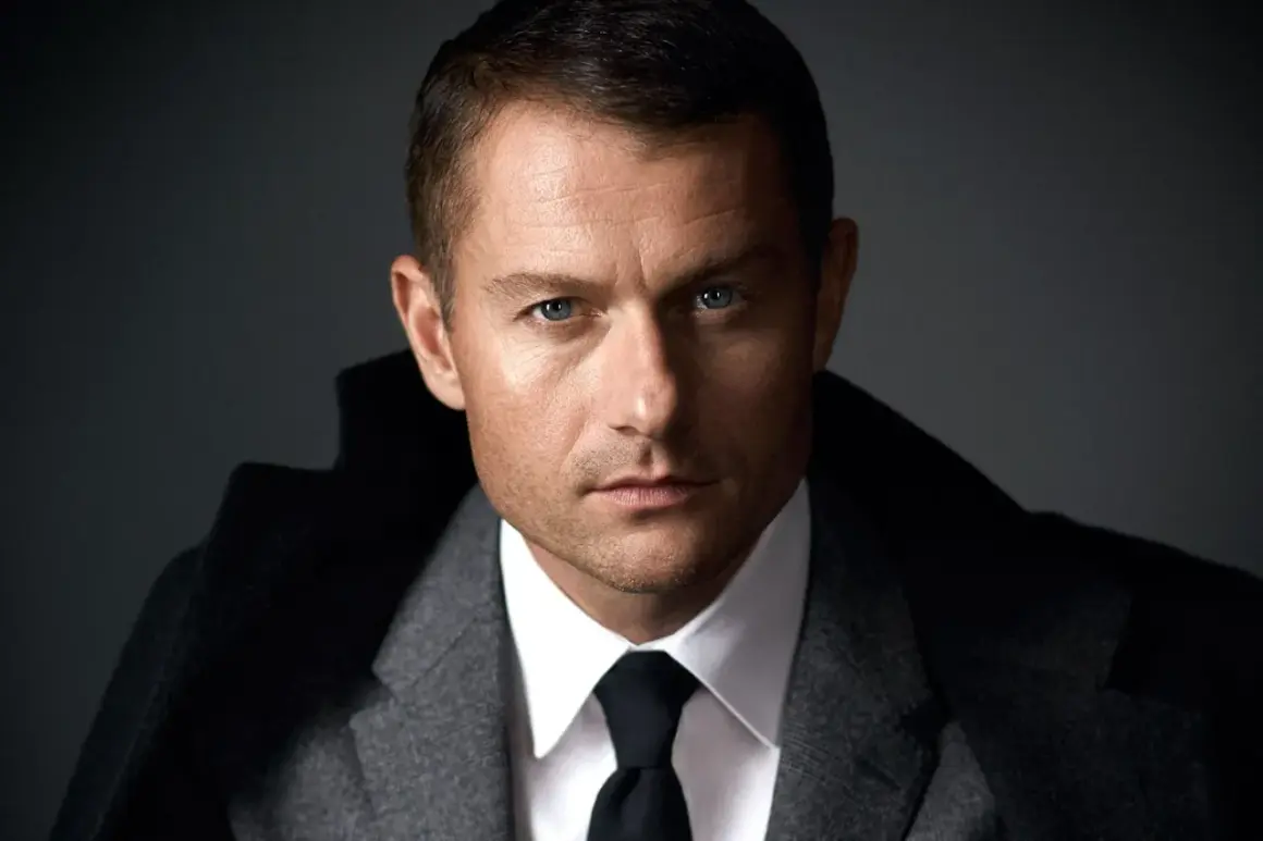 James Badge Dale w szarym garniturze i czarnym krawacie, z niebieskimi oczami wpatrującymi się w obiektyw.