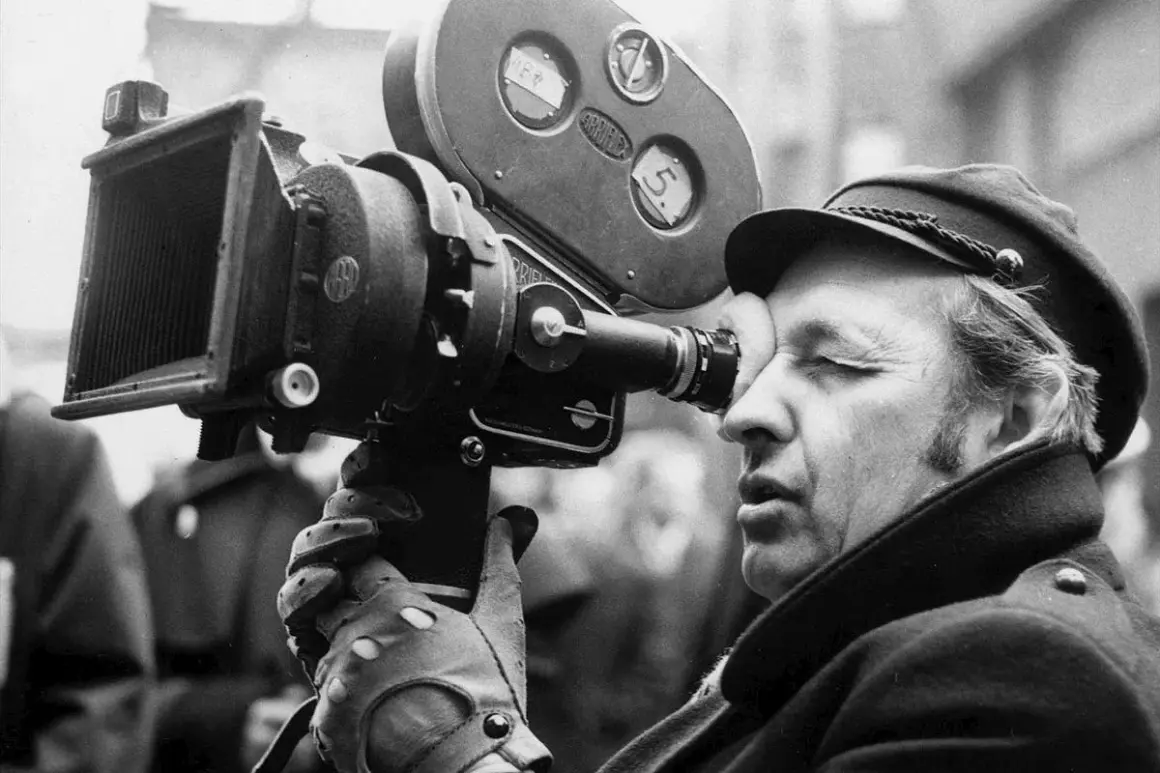 Andrzej Wajda patrzy przez wizjer kamery filmowej.