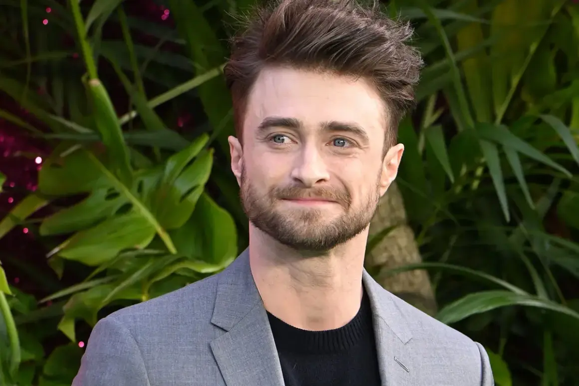 Daniel Radcliffe, który grał Harry'ego Pottera, w szarym garniturze na tle zieleni.