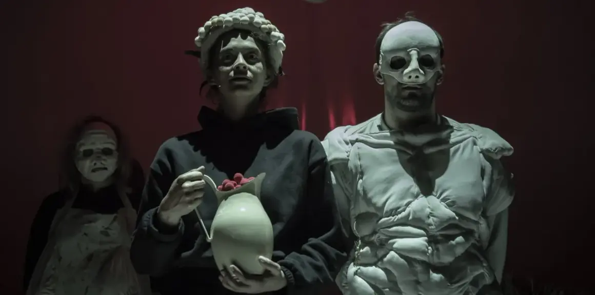 Trzy postacie w maskach na tle czerwonej kurtyny. Jedna z nich trzyma dzbanek z malinami. Scena z "Balladyny" w Teatrze Telewizji.