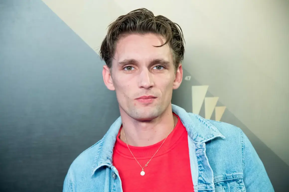 Filip Gurłacz, aktor, w czerwonej bluzie i jeansowej kurtce, z naszyjnikiem.