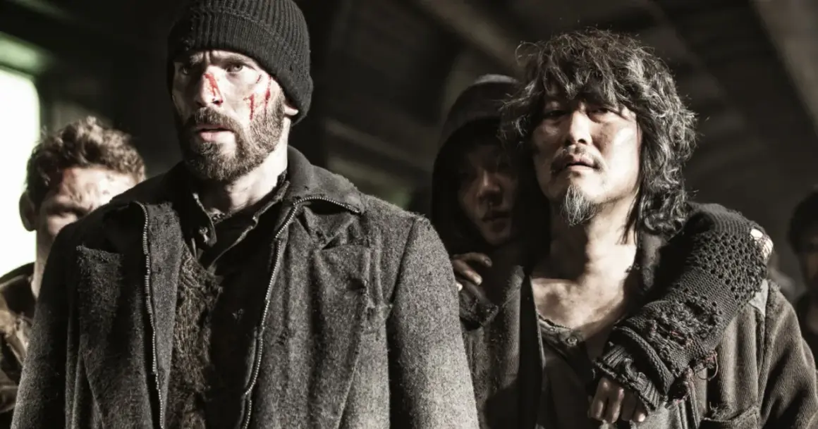Zraniona obsada Snowpiercer: Arka przyszłości, w tym Chris Evans, w surowych, postapokaliptycznych strojach.