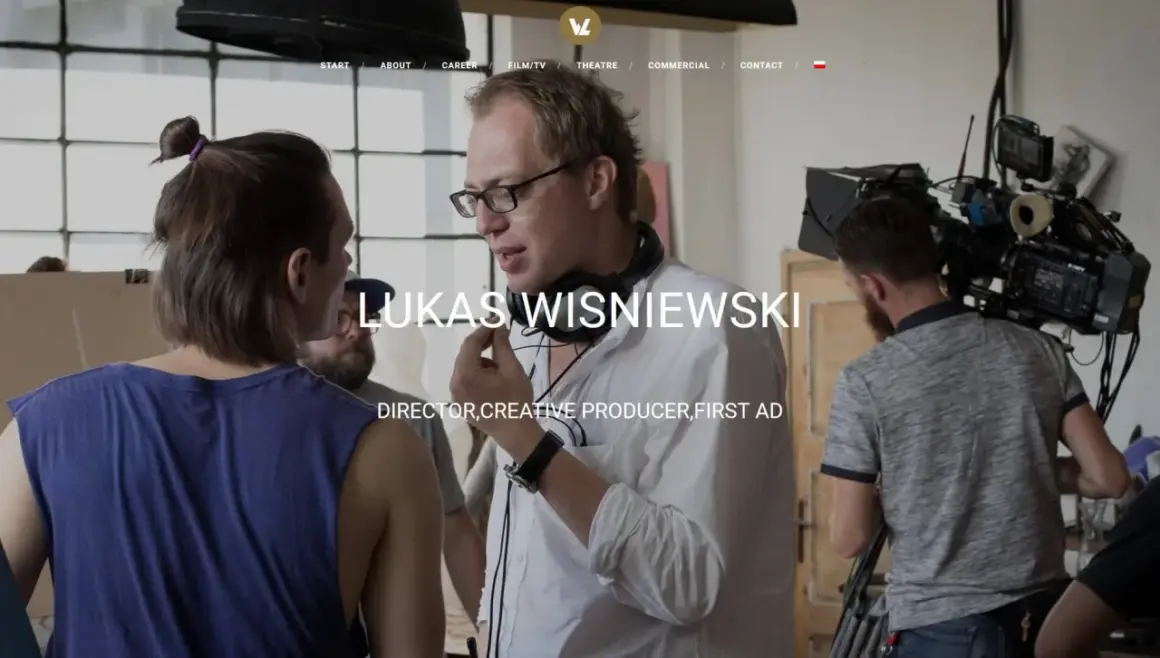 Łukasz Wiśniewski w białej koszuli z mikrofonem na szyi, na planie filmowym.