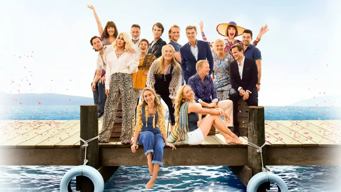 Obsada filmu "Mamma Mia!" na drewnianym molo z widokiem na morze.
