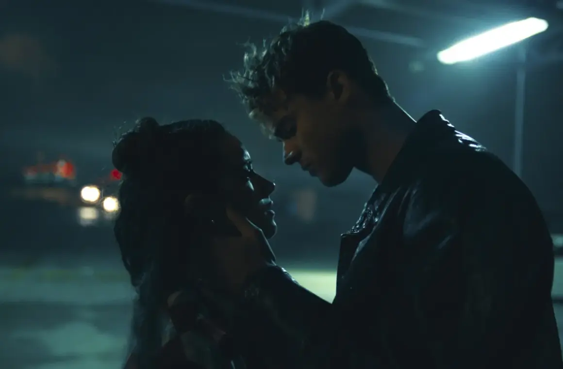 Nocna scena z filmu "The Kissing Booth". Elle i Noah w intymnym uścisku, w tle migoczące światła samochodów.