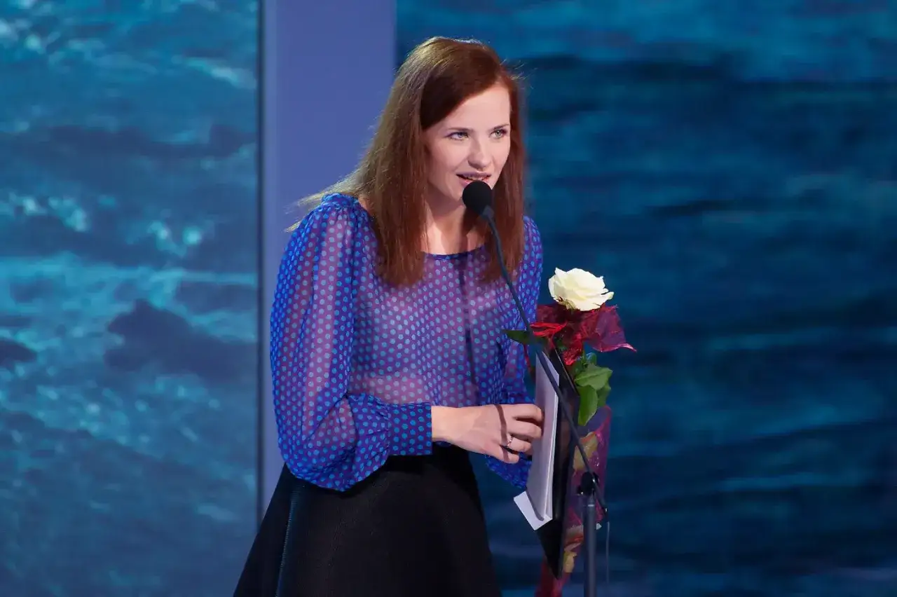 Wiktoria Gorodeckaja, której wzrost jest imponujący, przemawia do publiczności, trzymając różę i dokumenty.