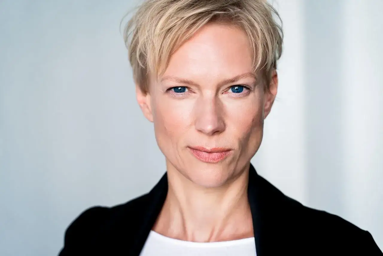 Portret Lise Risom Olsen z niebieskimi oczami i krótkimi blond włosami, w czarnej marynarce.
