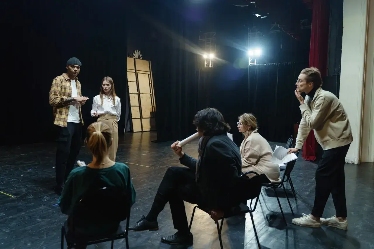 Aktorzy na próbie dyskutują o tym, ile zarabia aktor miesięcznie, analizując scenariusz na scenie teatralnej.