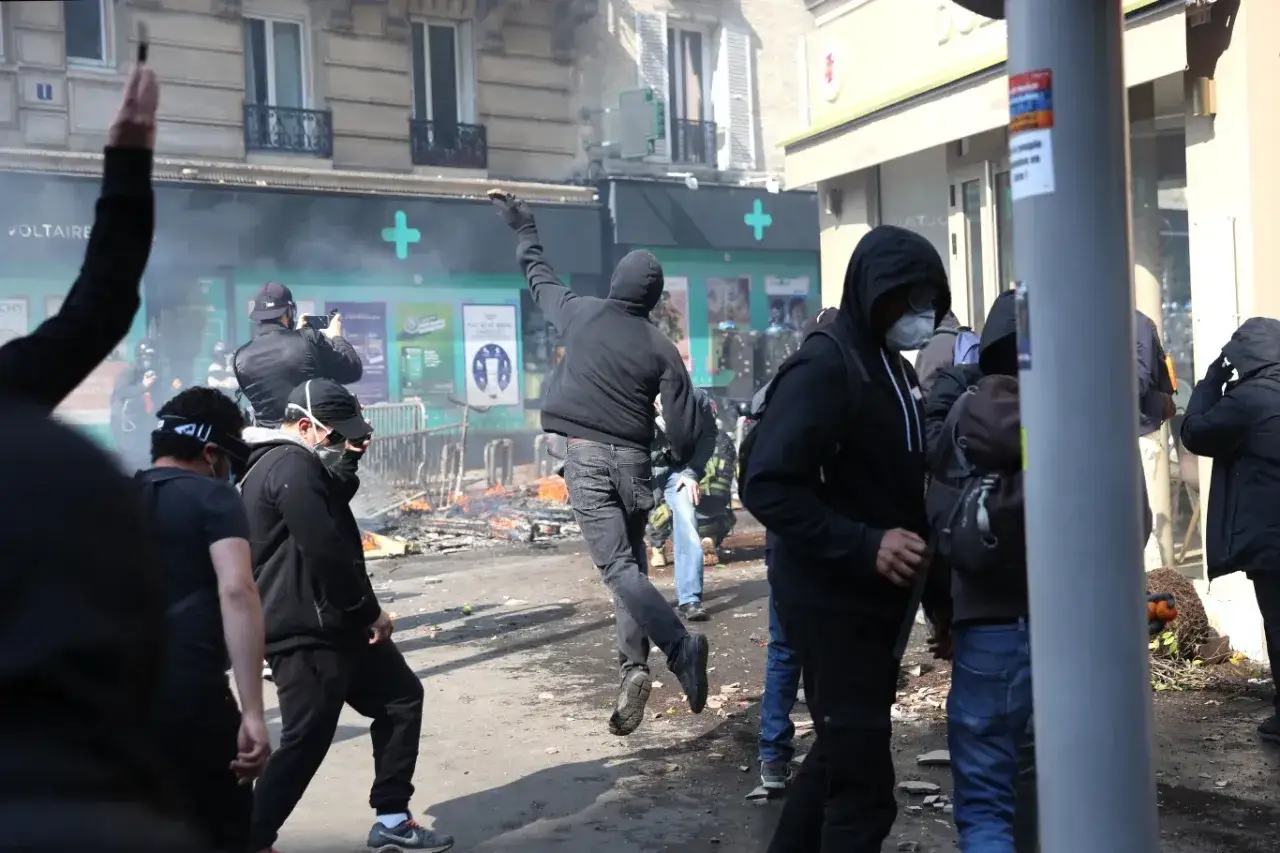 Paryż w ogniu: protestujący w maskach i kapturach rzucają przedmiotami, płoną zniszczenia.