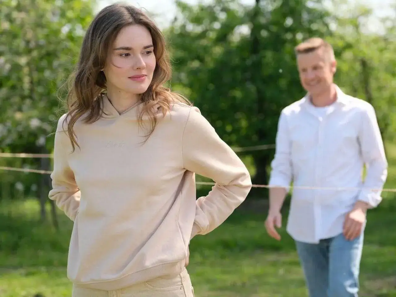 Czy Dominika Kachlik odchodzi z M jak Miłość? Młoda kobieta w beżowej bluzie i mężczyzna w białej koszuli na tle zieleni.