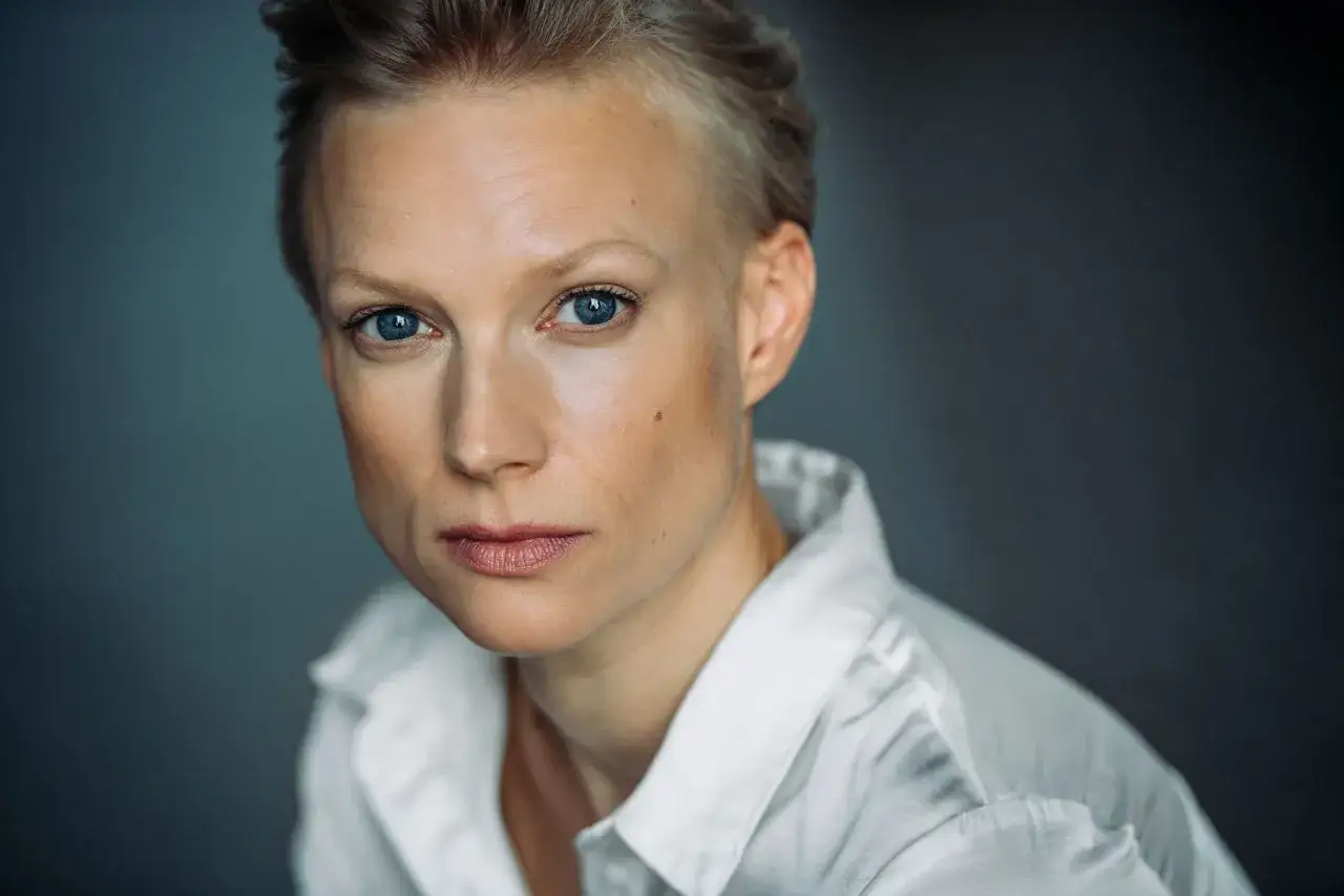 Portret Lise Risom Olsen z niebieskimi oczami i krótkimi blond włosami, w białej koszuli.