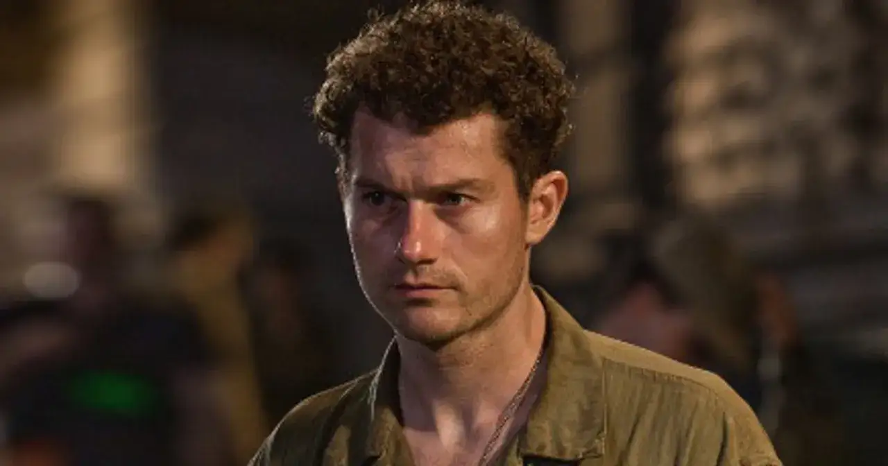 James Badge Dale z kręconymi włosami, w wojskowej koszuli, patrzy z uwagą.