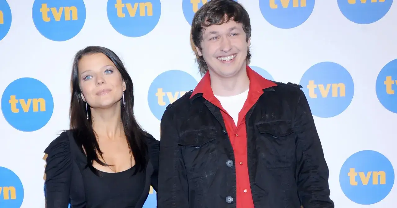 Aktorzy na wspólnej, uśmiechnięty mężczyzna w czarnej kurtce i czerwonej koszuli obok kobiety z długimi ciemnymi włosami, na tle logo TVN.