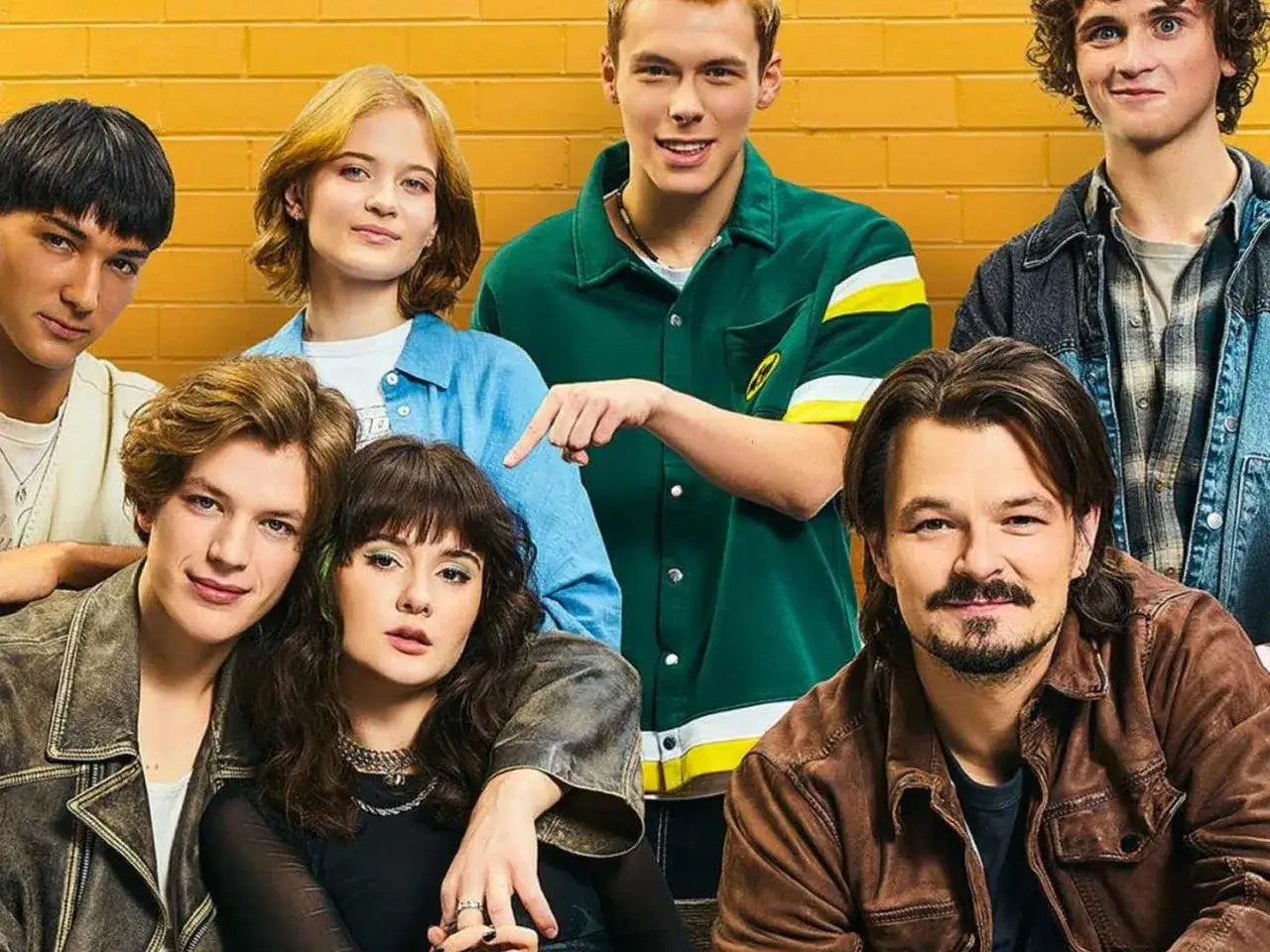 Grupa młodych ludzi pozuje do zdjęcia. Jeden z nich, w zielonej bluzie, wskazuje palcem, jakby chciał powiedzieć: