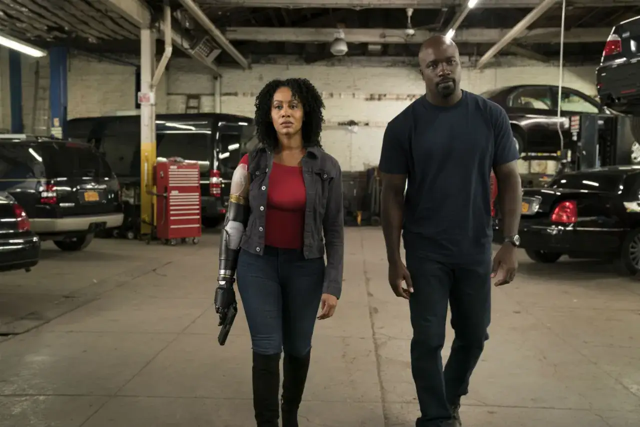 Luke Cage obsada: Misty Knight z protezą ręki i Luke Cage idą przez warsztat samochodowy.