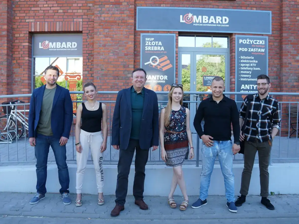 Aktorzy z lombardu pozują przed budynkiem.
