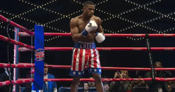 Michael B. Jordan jako Adonis Creed w szortach w barwach USA, gotowy do walki. W tle widać Sylvestra Stallone. Creed II obsada w akcji.