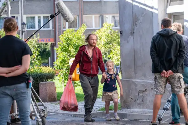 Mężczyzna z dziewczynką idą ulicą, za nimi ekipa filmowa z mikrofonem.