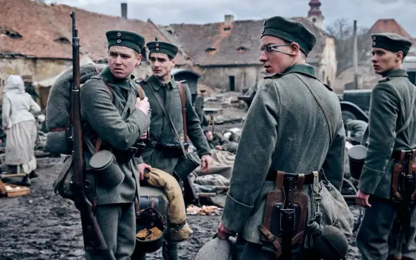 Żołnierze w mundurach z I wojny światowej, z karabinami i plecakami, stoją na błotnistym podwórzu. Na zachodzie bez zmian obsada.