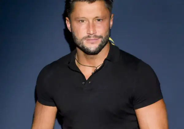Piotr Mróz w czarnej koszulce polo, z zarostem i naszyjnikiem.