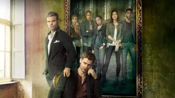 Grupowe zdjęcie obsady "The Originals" w stylizowanych strojach. W pierwszym planie siedzi Klaus, a za nim stoi Elijah. W tle, w ramie obrazu, widać pozostałych członków rodziny.